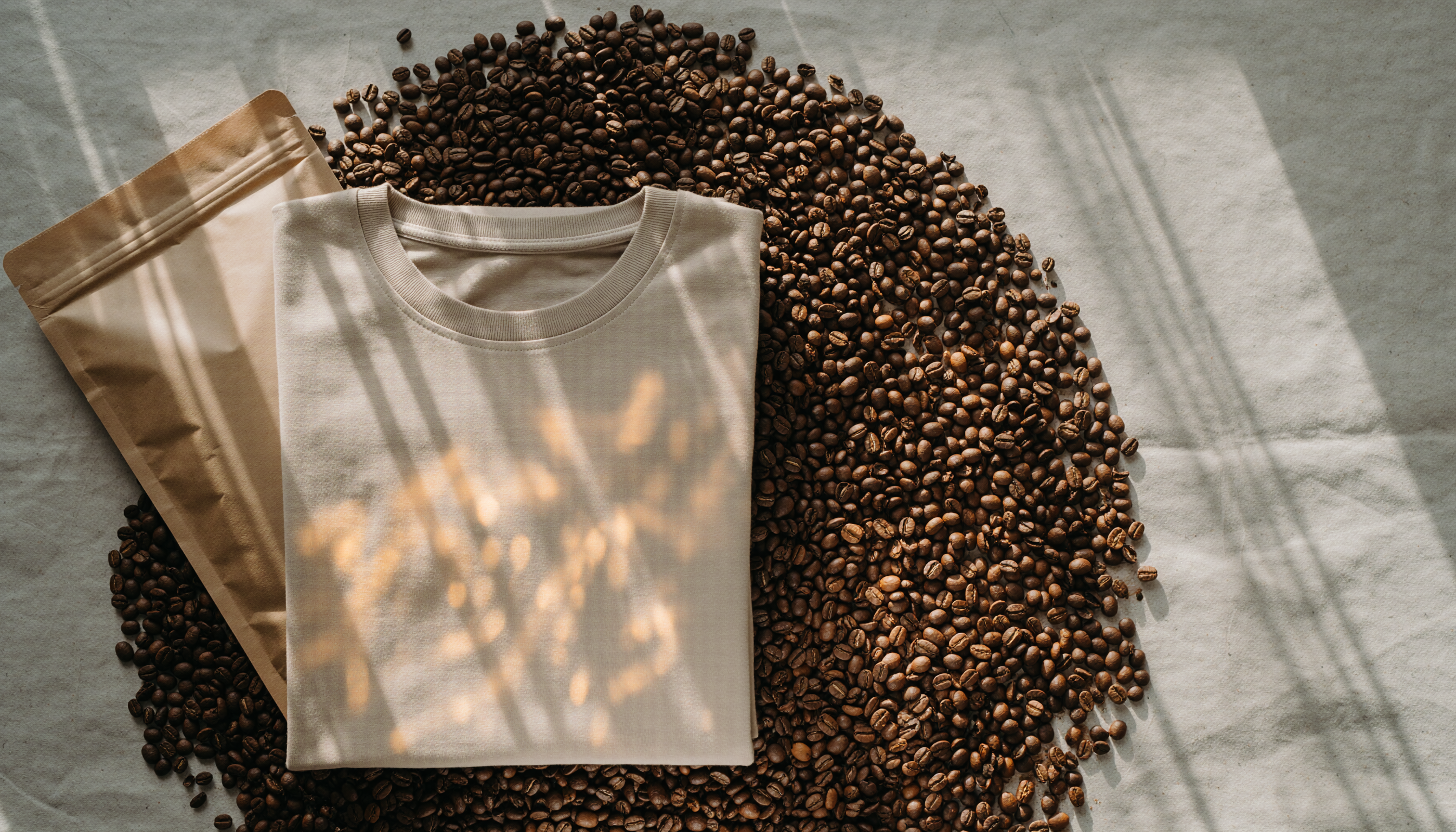 beige T-shirt og en kaffepose ligger påp en bunke af kaffebønner